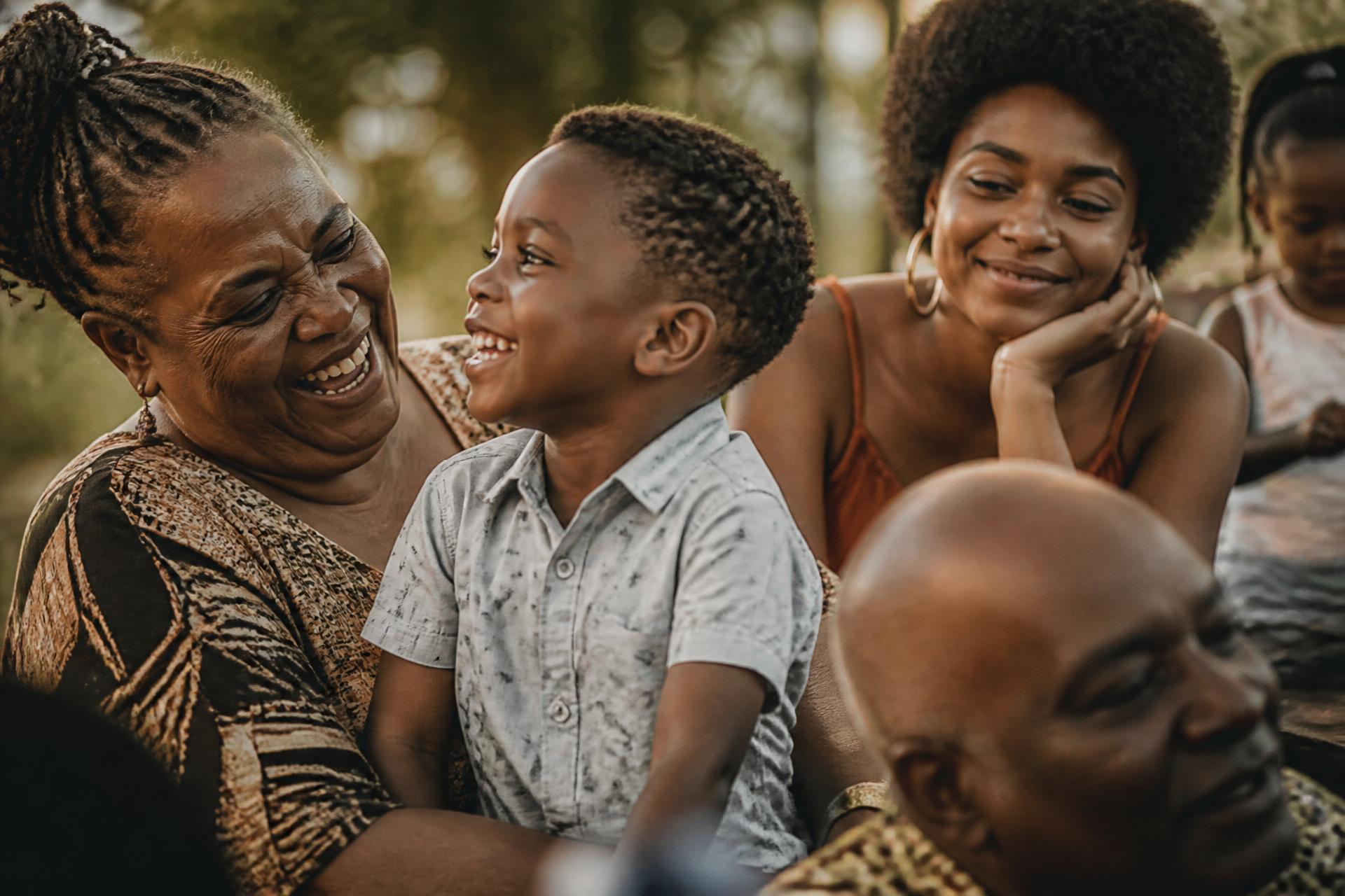 Three generations of a Black family laughing together outdoors in warm evening light